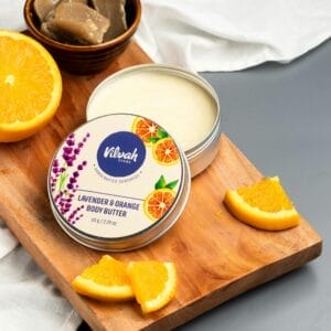 High-angle view of lavender and orange body butter with fresh orange slices on a wooden tray.